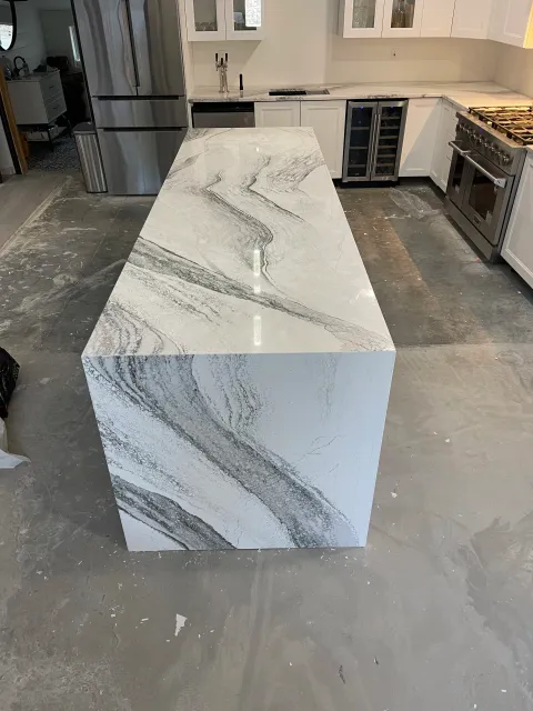 Kitchen with white cabinets, stainless steel refrigerator, black dishwasher, and a large marble kitchen island with gray veining.