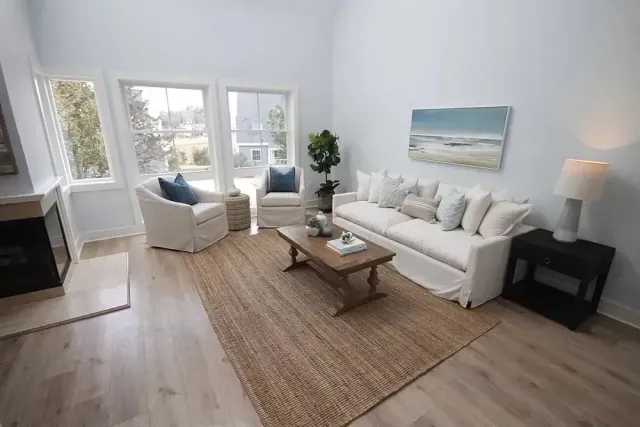 A bright living room features a white sofa, two armchairs, a wooden coffee table, and a rug on light wood floors.