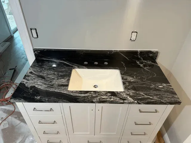 Bathroom vanity with black marble countertop, white sink, and white cabinet drawers being installed