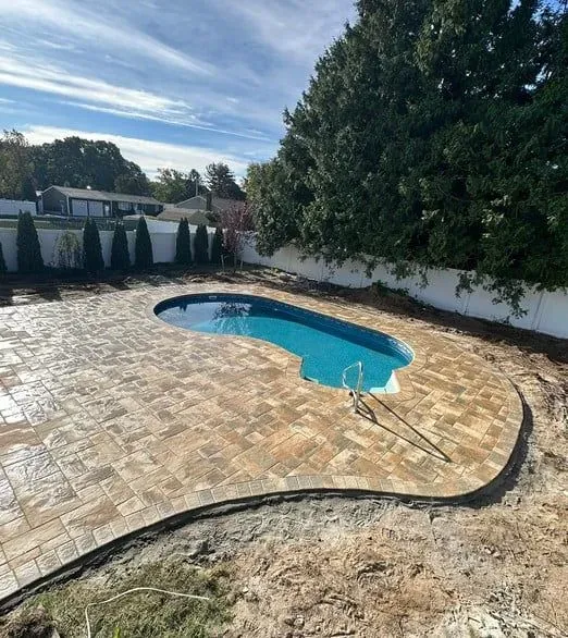 A large swimming pool is surrounded by a brick patio