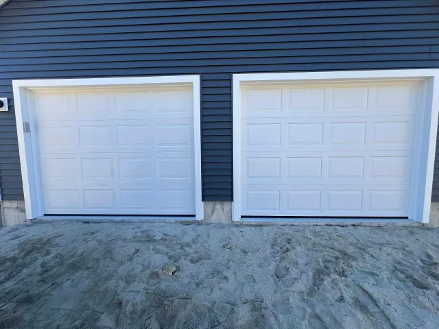 Two white garage doors with white trim, set in a blue house facade, against a gray mound.