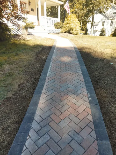 Brick walkway leading to a white house porch through a sunlit yard