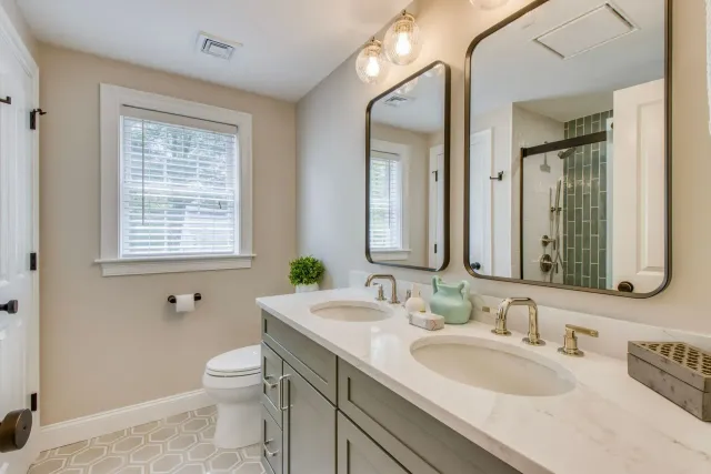 Bright modern bathroom with double vanity, large mirror, window, and glass shower door
