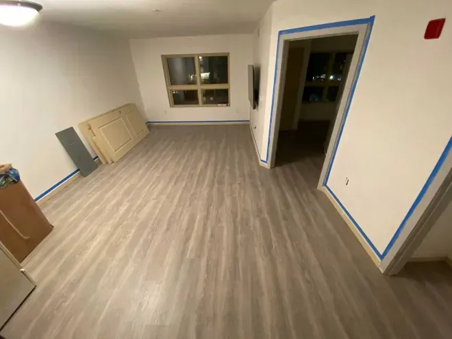 Empty room with wood-look flooring, white walls, and blue painter's tape around a doorway and baseboards.