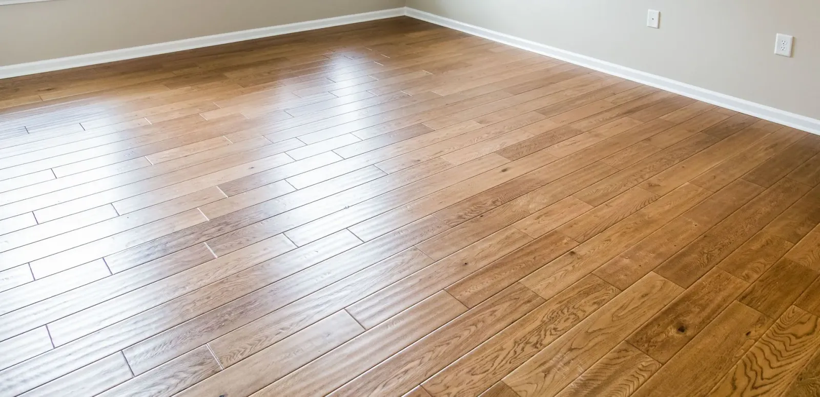Wooden flooring in a room with white baseboards and light gray walls.