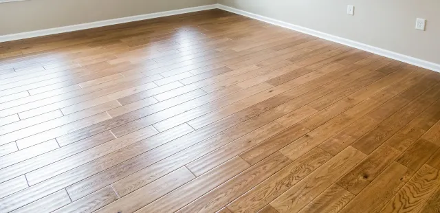 Wooden flooring in a room with white baseboards and light gray walls.