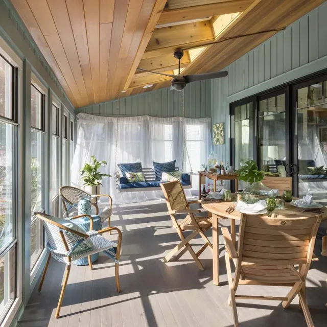 A sun room with a couch , chairs , tables and a ceiling fan.