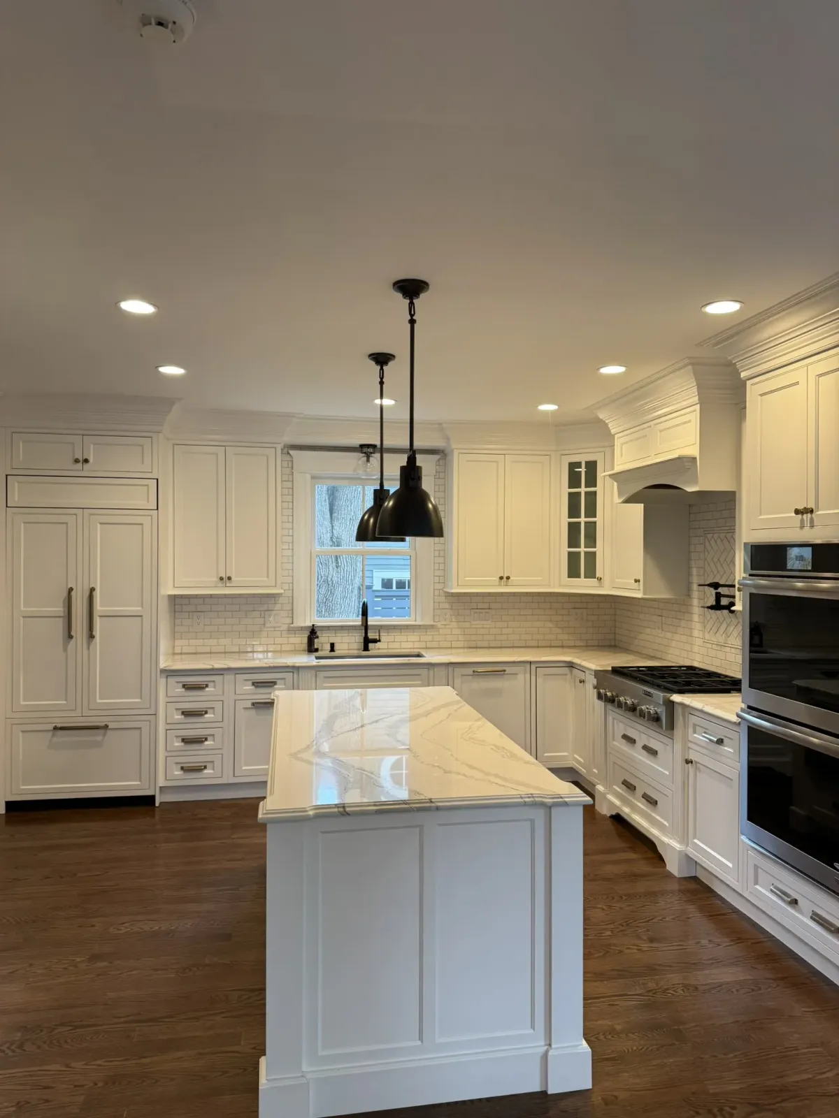 White custom kitchen cabinetry with a marble-top island, paneled refrigerator surround and a fitted range hood
