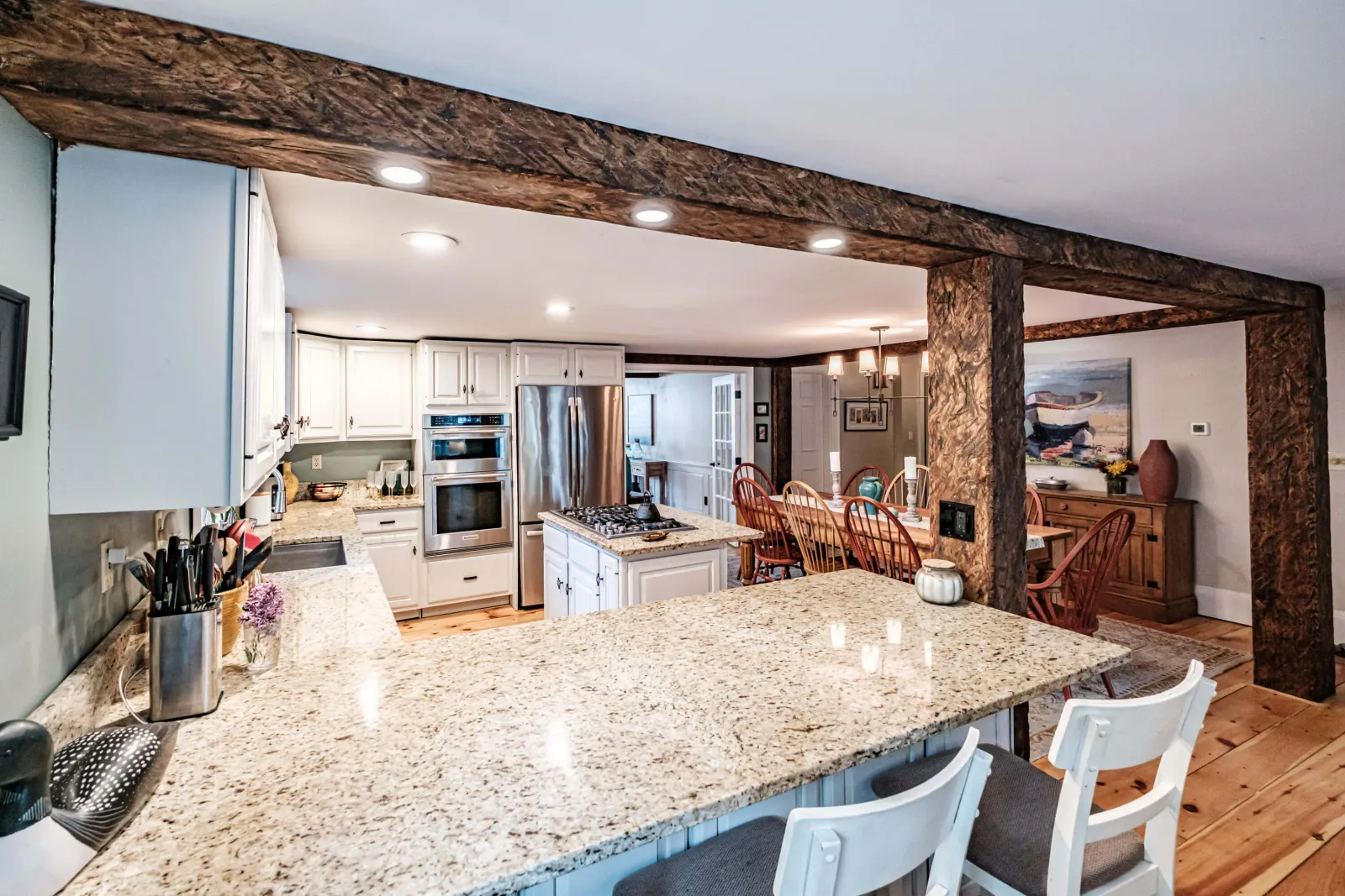 Kitchen with granite counters, white cabinets, wooden beams, stainless steel fridge, and a dining table with chairs.