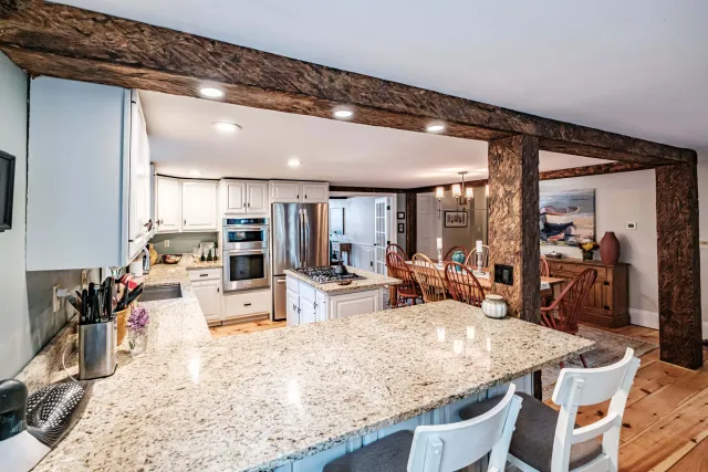 Kitchen with granite counters, white cabinets, wooden beams, stainless steel fridge, and a dining table with chairs.