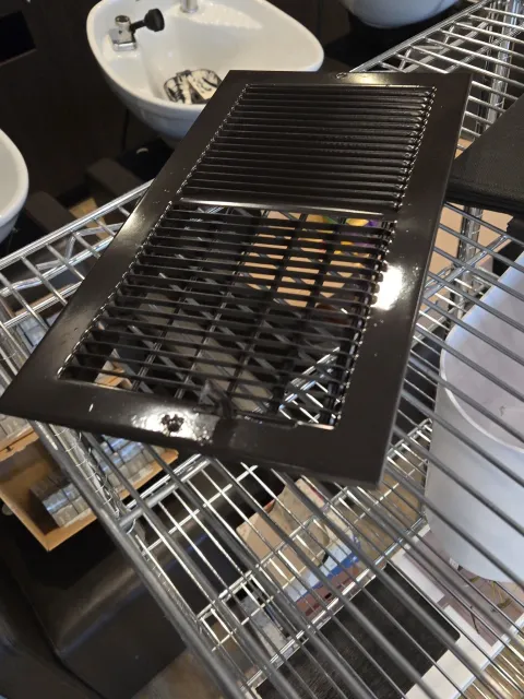 Black metal grate resting on a wire shelf above a sink with bowls and kitchen items nearby