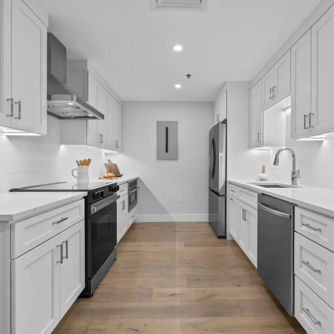 A modern, empty kitchen with white cabinets, stainless steel appliances, and light wood flooring.