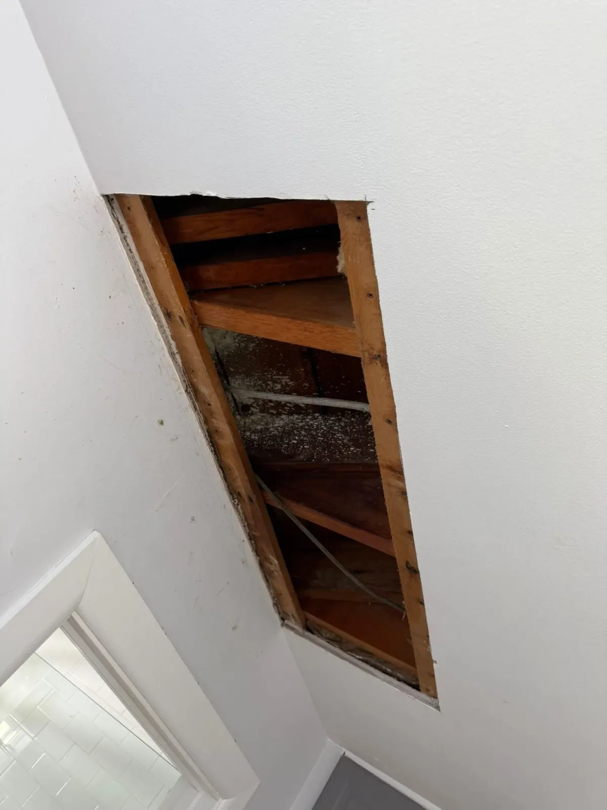 Open ceiling with exposed wooden beams and insulation near a skylight inside a white room
