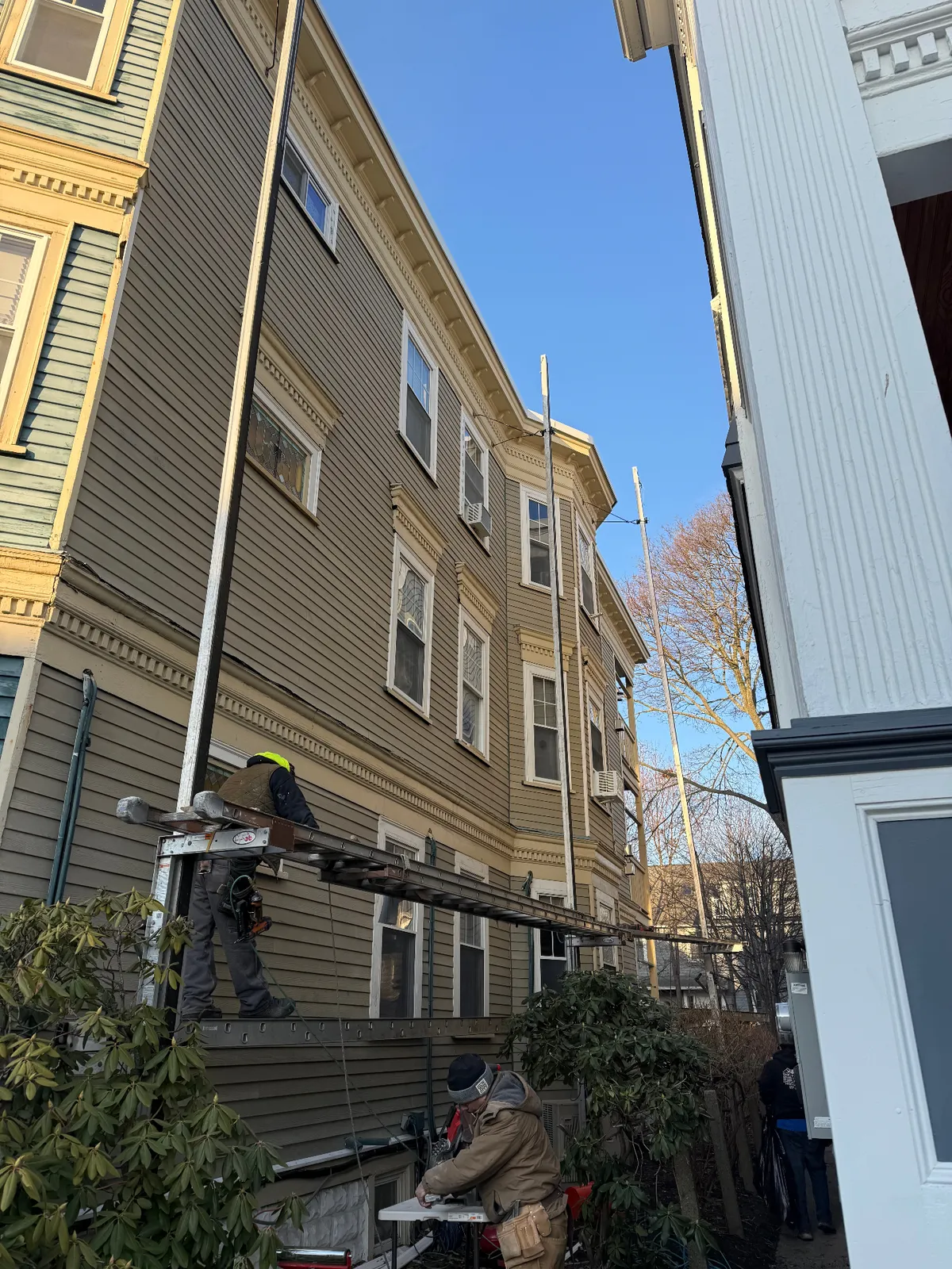 Dan's Painting & General Contracting crew on ladder jacks installing and prepping siding on a tall Victorian multi-family in Boston, MA