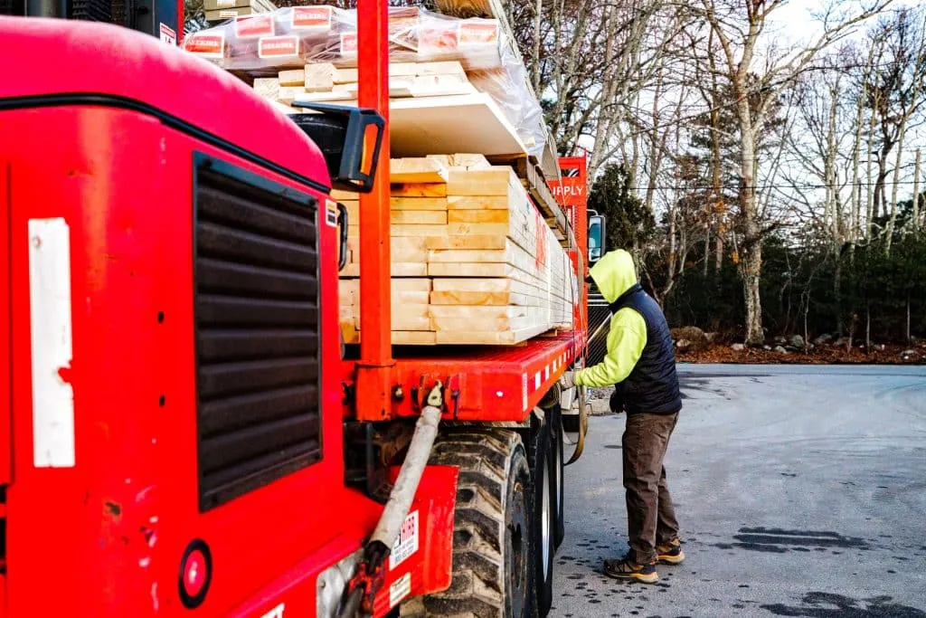 Delivery truck loaded with lumber and building materials, worker preparing for unloading, emphasizing Dartmouth Building Supply's reliable delivery service for construction professionals.