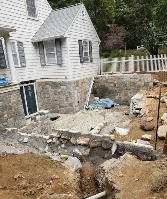 House with a dug-up stone foundation and construction debris in the yard