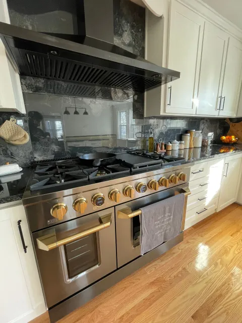 Bright kitchen with stainless steel gas range, black hood, white cabinets, and hardwood floor