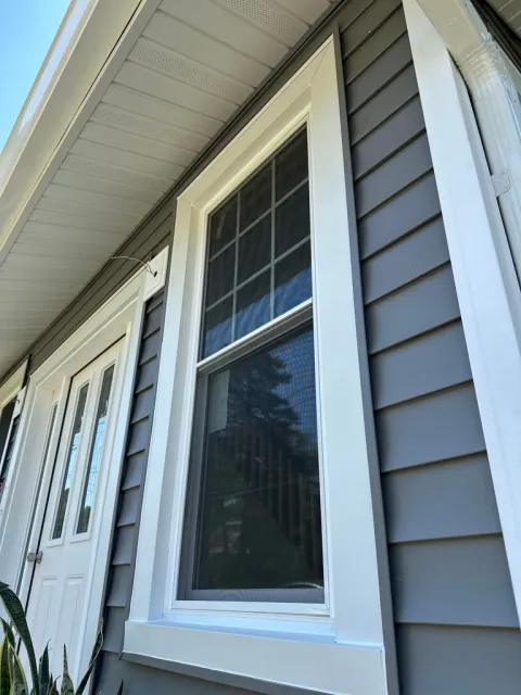 Modern house exterior with white trim windows and gray horizontal siding, clear blue sky visible