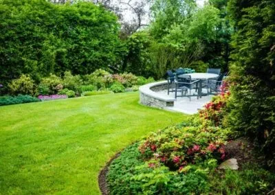 Lush backyard with green grass, shaded trees, and a stone patio maintained by Massachusetts lawn care expert Jon Sneider.