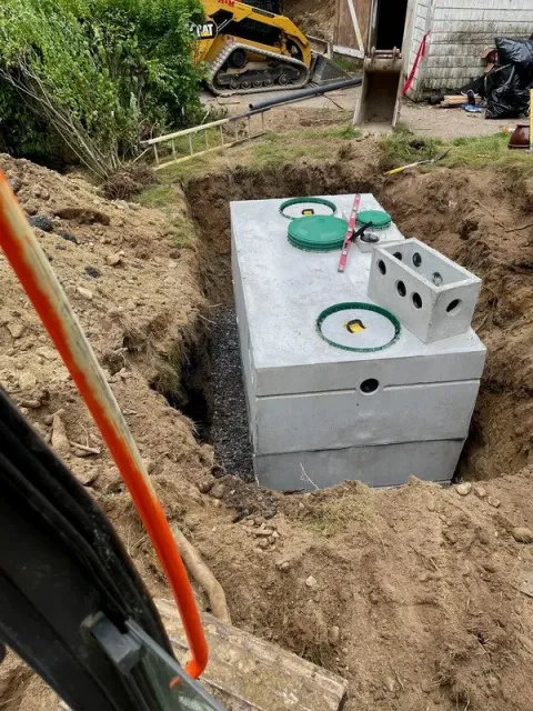An Elgen Septic Tank is being installed in an excavated trench, surrounded by soil, with construction tools and equipment nearby.