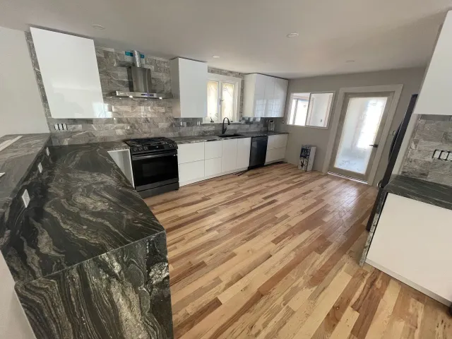 Modern kitchen with white cabinets, dark countertops, and hardwood floors.