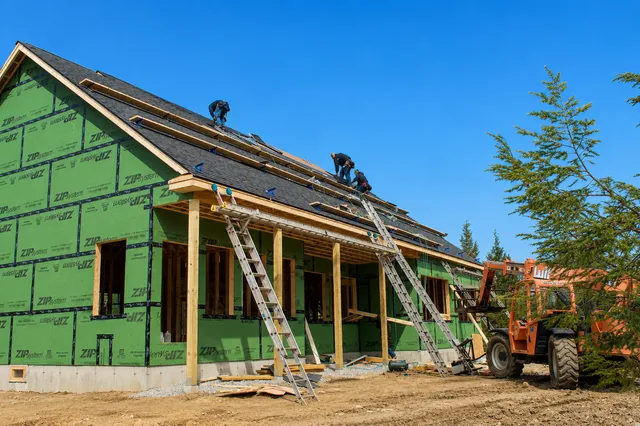 Custom home jobsite wrapped in weather barrier with equipment on site