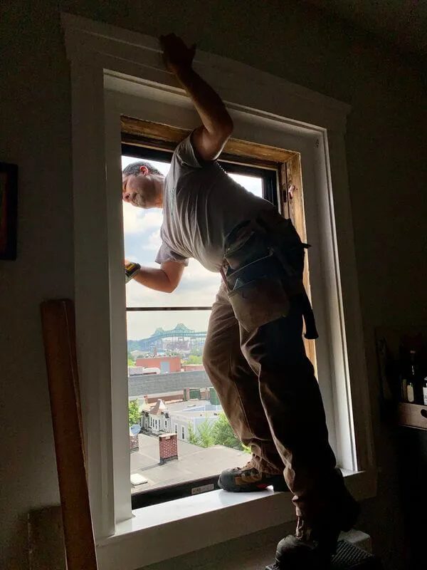 Installer securing trim around a window with a city view, tool belt around his waist