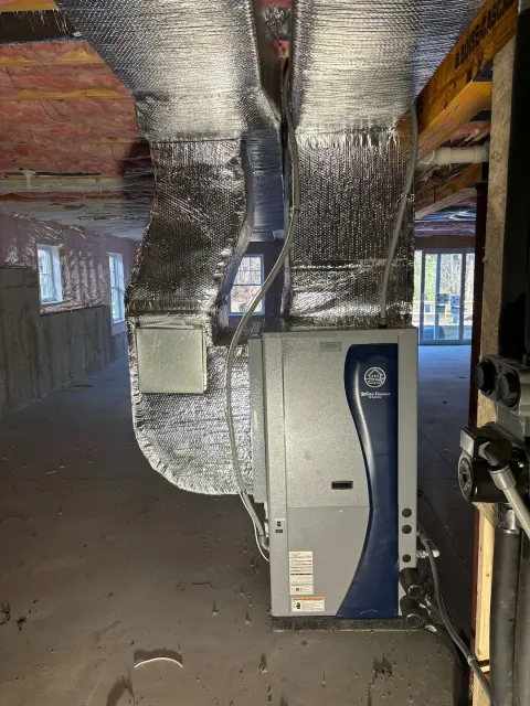 Basement HVAC unit with silver ductwork and blue paneling in a partially finished room.