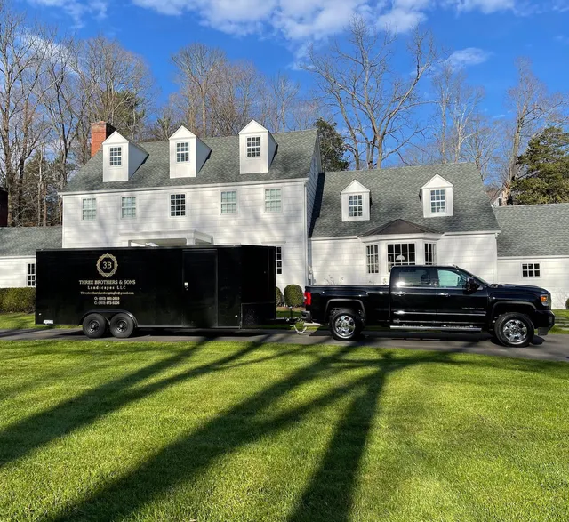 A black truck is towing a black trailer in front of a large white house