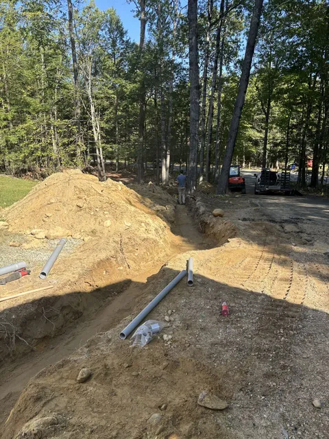 Service conduit stubbing up out of a freshly dug trench beside the spoil pile