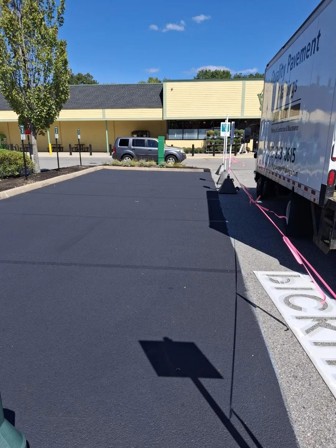 Freshly paved dark asphalt parking lot beside a building and a parked moving truck on a sunny day