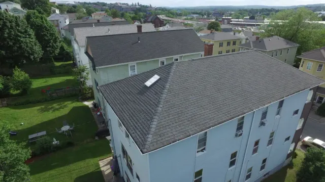 Aerial view of white apartment buildings with gray roofs and green lawns in a suburban neighborhood