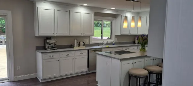 Bright kitchen with white cabinets, gray counters, window, sink, and three pendant lights over a peninsula.