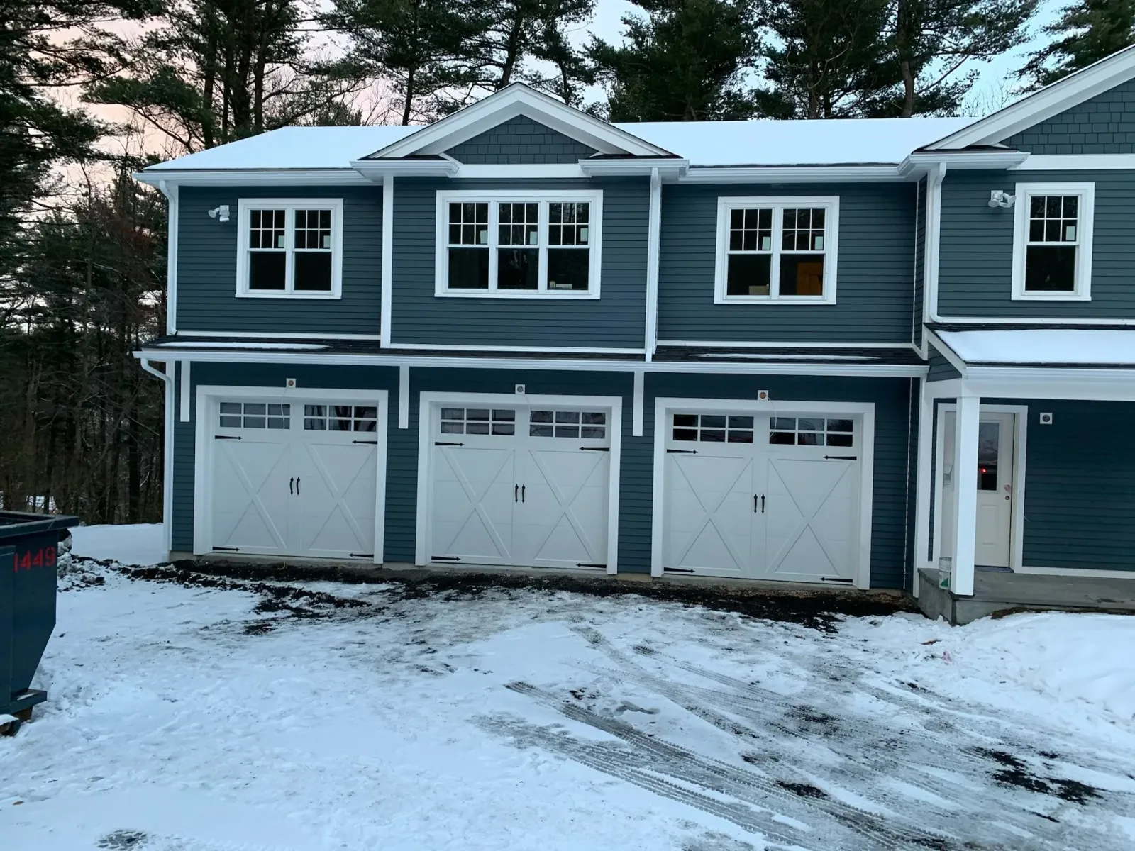 A blue house with white garage doors is covered in snow