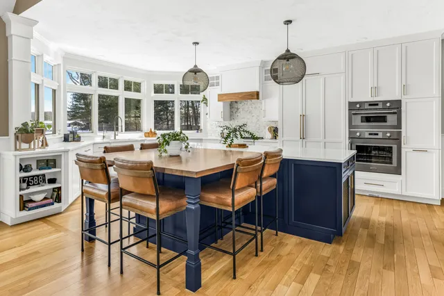 White kitchen with navy blue island, leather barstools, and pendant lighting