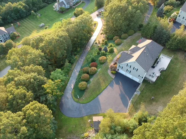 Aerial photo of a freshly sealcoated residential driveway in Hardvard MA with dark black finish, surrounding lawn, and clear contrast showing professional asphalt maintenance.