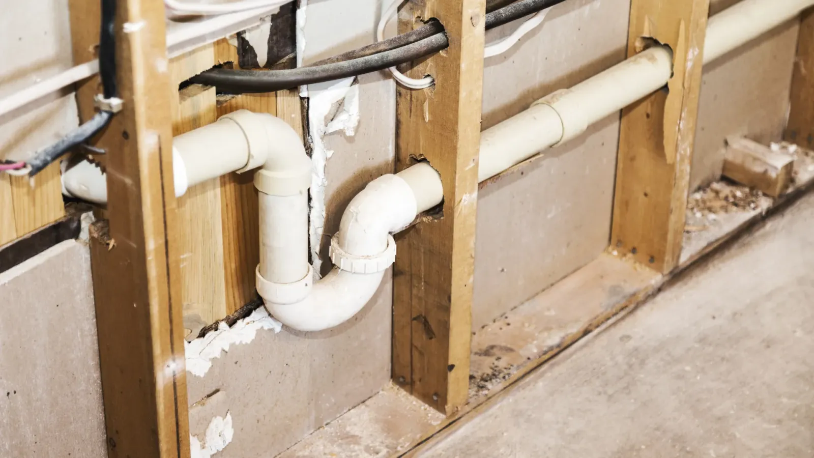 Plumbing drain pipes visible inside wall studs. White plastic pipes, wood framing, neutral color.