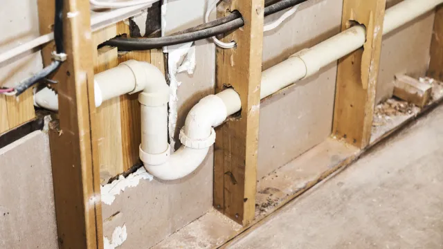 Plumbing drain pipes visible inside wall studs. White plastic pipes, wood framing, neutral color.