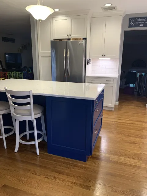 A kitchen with a blue island , white cabinets , stools and a refrigerator.