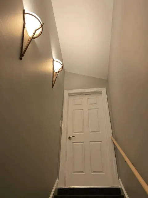 Stairwell with two wall lights, a wooden handrail, and a white door at the landing.