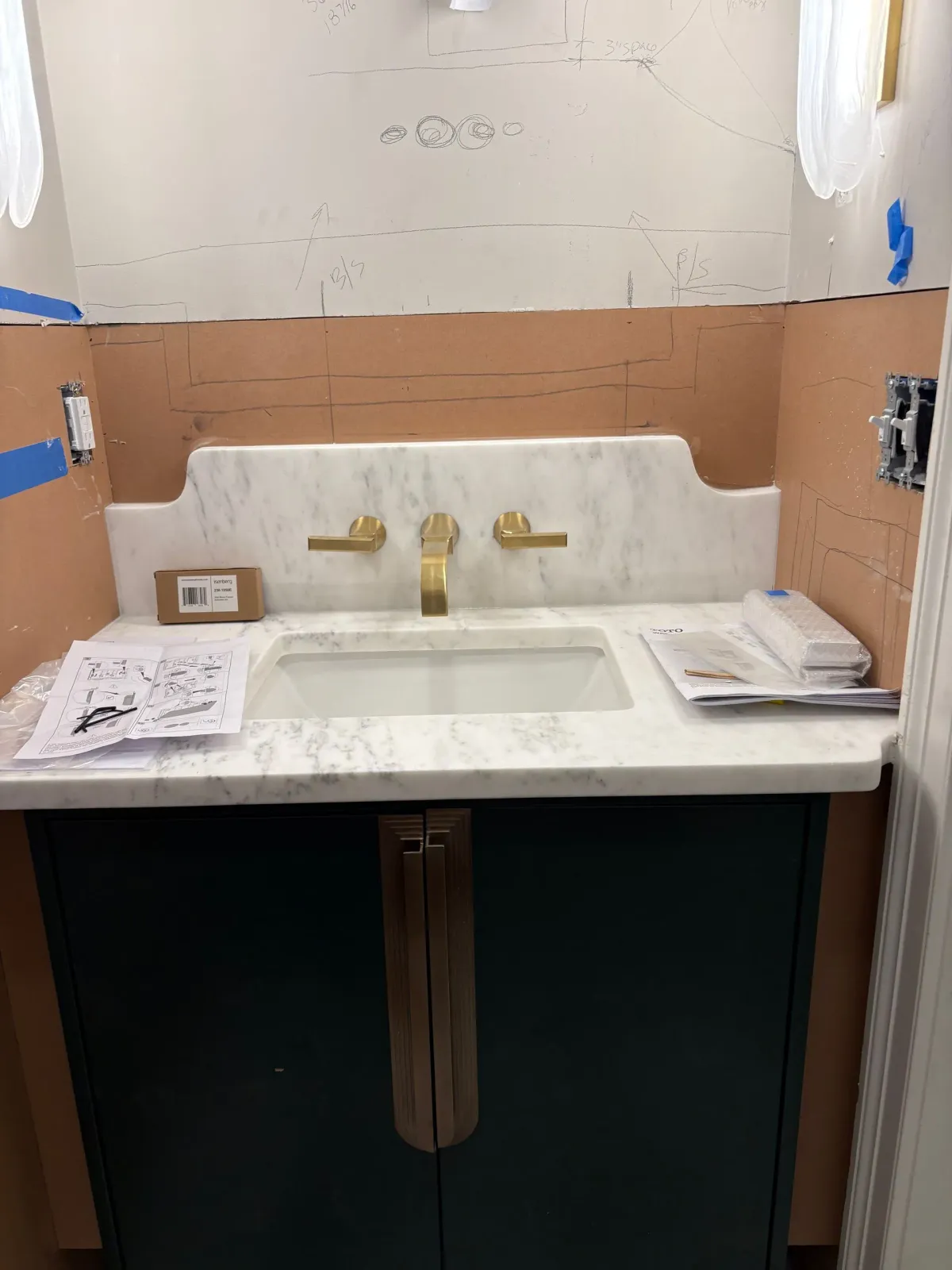Bathroom vanity with a dark green cabinet, marble countertop, and gold fixtures.
