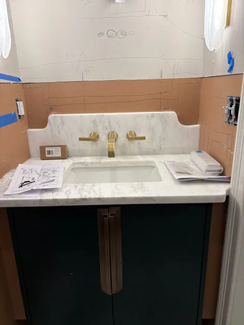 Bathroom vanity with a dark green cabinet, marble countertop, and gold fixtures.