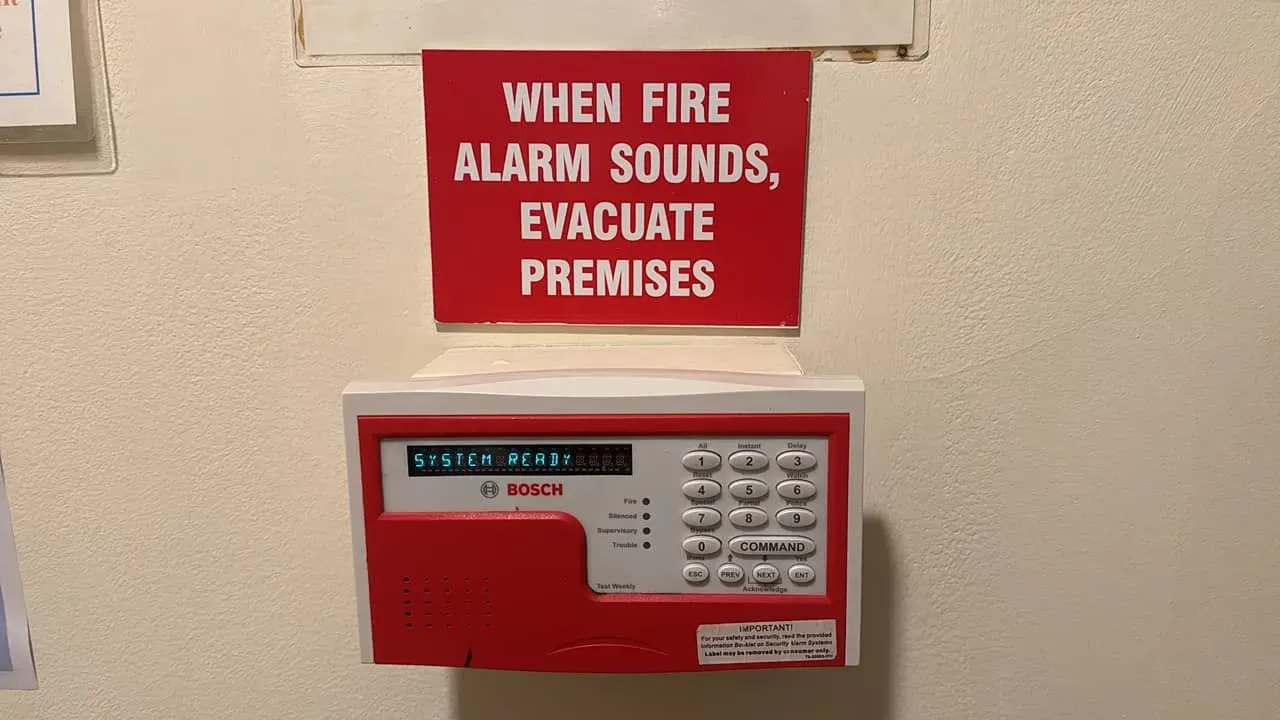 Red fire alarm control panel with instructions to evacuate premises, mounted on a wall.