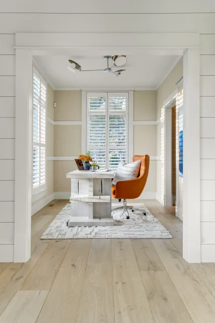 Hardwood floor refinishing in a Hingham home office featuring a white desk, an orange chair, white plantation shutters, and soft neutral walls.