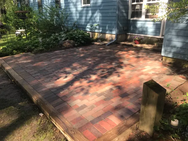 brick patio with wooden border next to a blue house