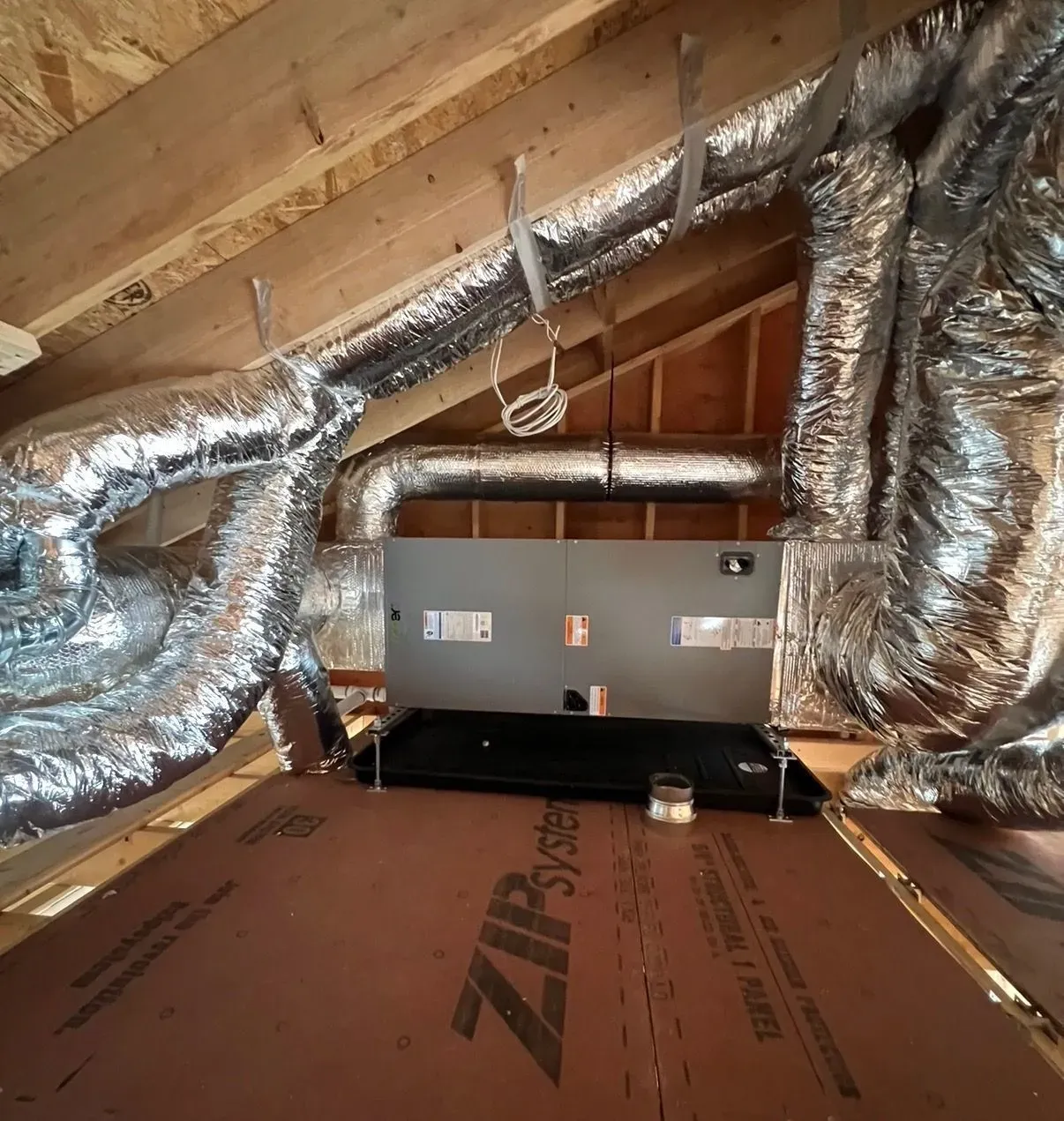 Attic with silver HVAC ducts, a central metal unit, and brown insulation panels on the floor