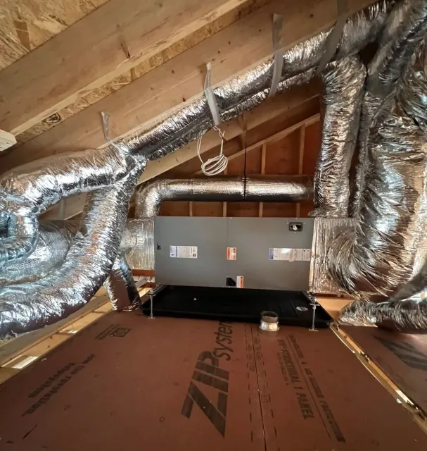 Attic with silver HVAC ducts, a central metal unit, and brown insulation panels on the floor