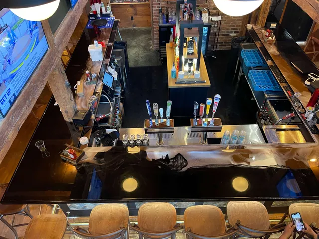 Empty bar counter with beer taps, glasses, wooden stools, and a TV showing a sports program.
