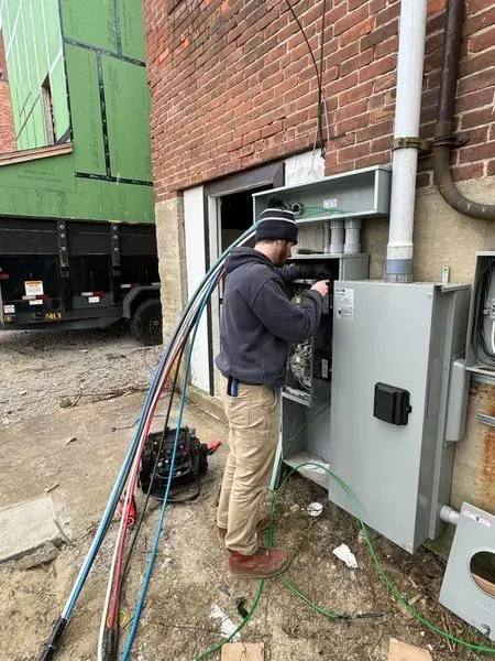 Electrician working on a circuit breaker panel with wires and a screwdriver.
