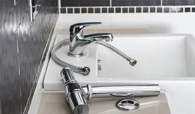 A sink with a detached chrome faucet and hoses placed on the countertop, in front of a tiled black and white wall, indicating ongoing plumbing or faucet installation.